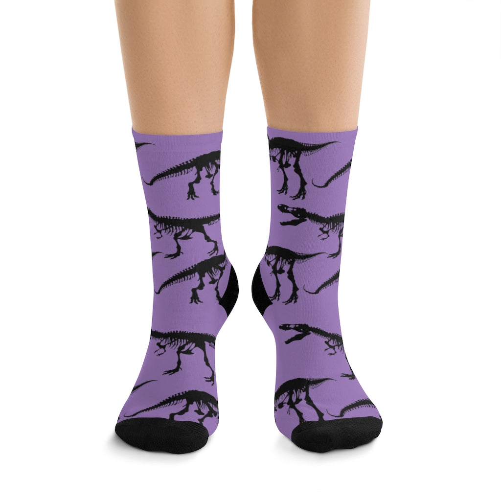 A woman wearing a pair of purple dinosaur socks featuring black skeleton outlines of a t-rex. 