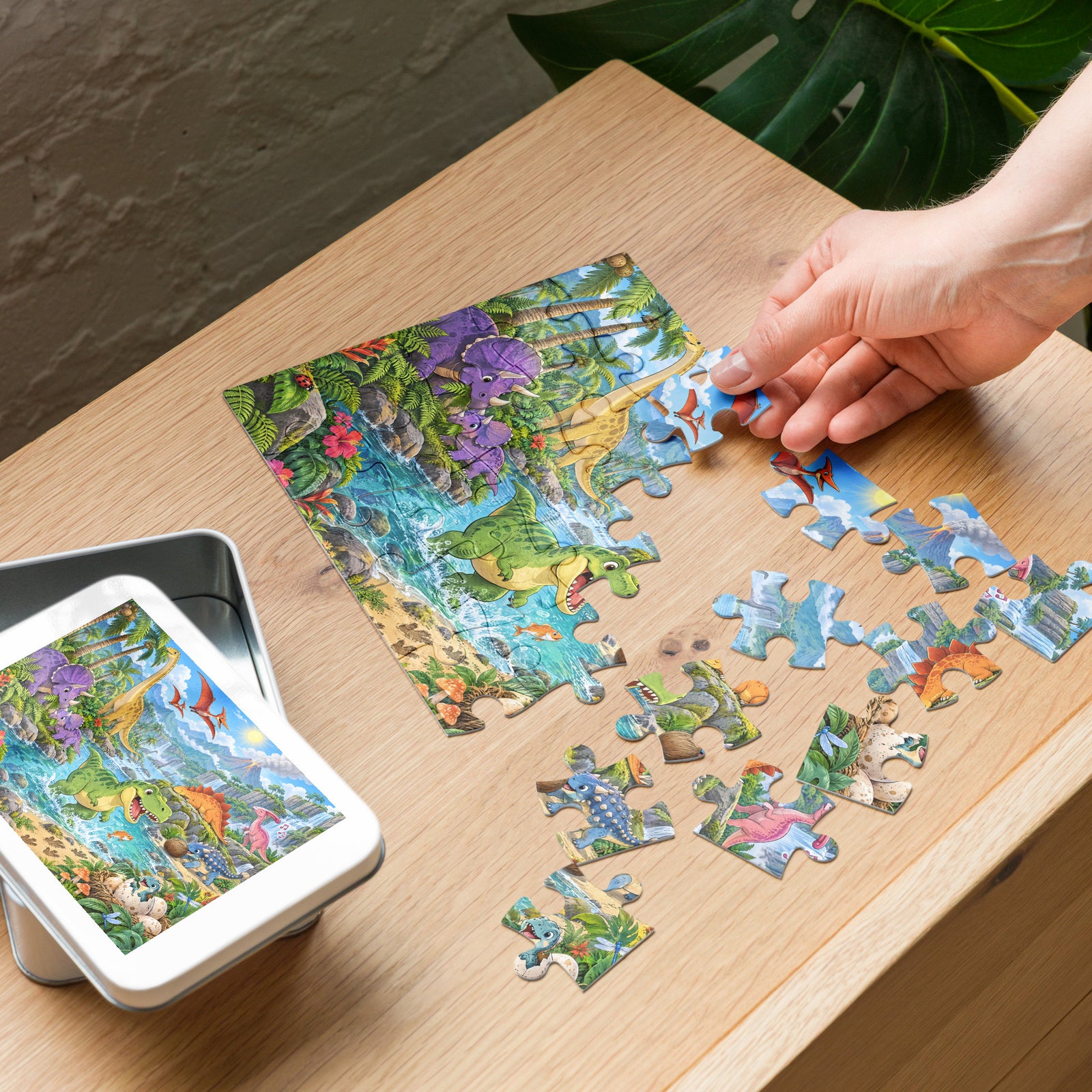 Building the Dino Valley dinosaur puzzle on a table next to its white metal gift tin with the picture on the lid