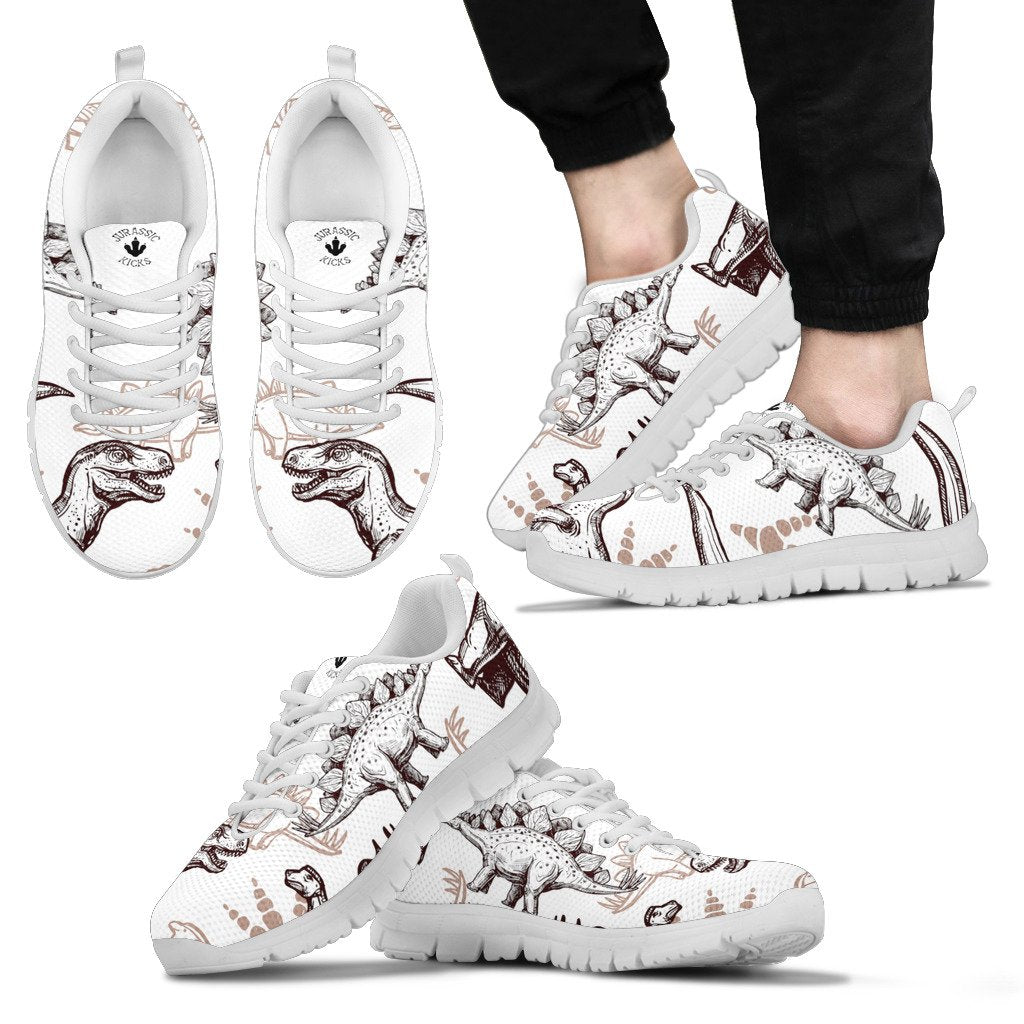 Kid wearing a pair of dinosaur shoes with brown stenciled dinosaurs on a white base. Featuring T-Rex and Stegosaurus. 