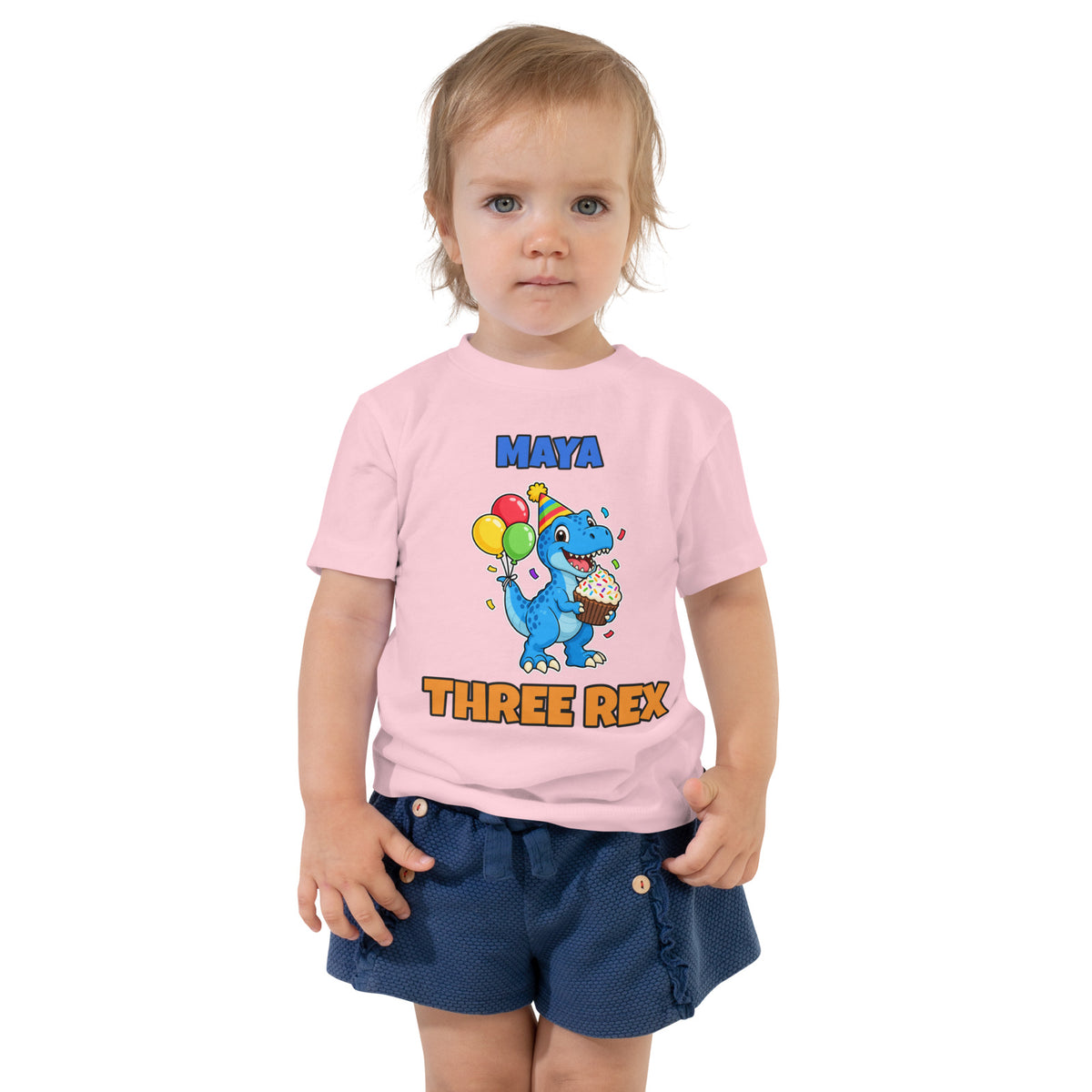 Birthday Rex personalized toddler dinosaur birthday t-shirt in Pink, blue party-hat T-rex with cupcake and balloons between the name MAYA and THREE REX, worn by a child, front view
