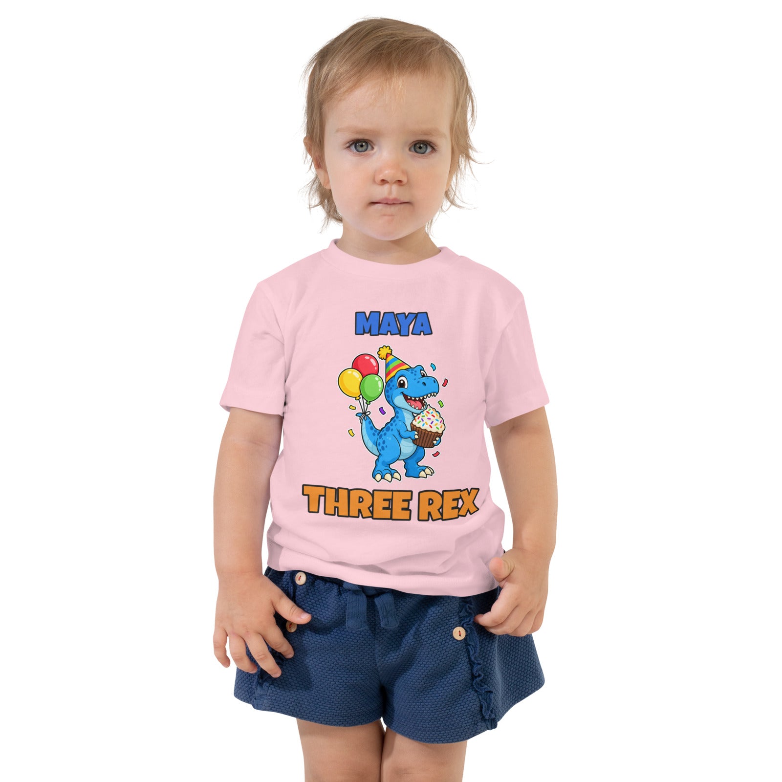 Birthday Rex personalized toddler dinosaur birthday t-shirt in Pink, blue party-hat T-rex with cupcake and balloons between the name MAYA and THREE REX, worn by a child, front view