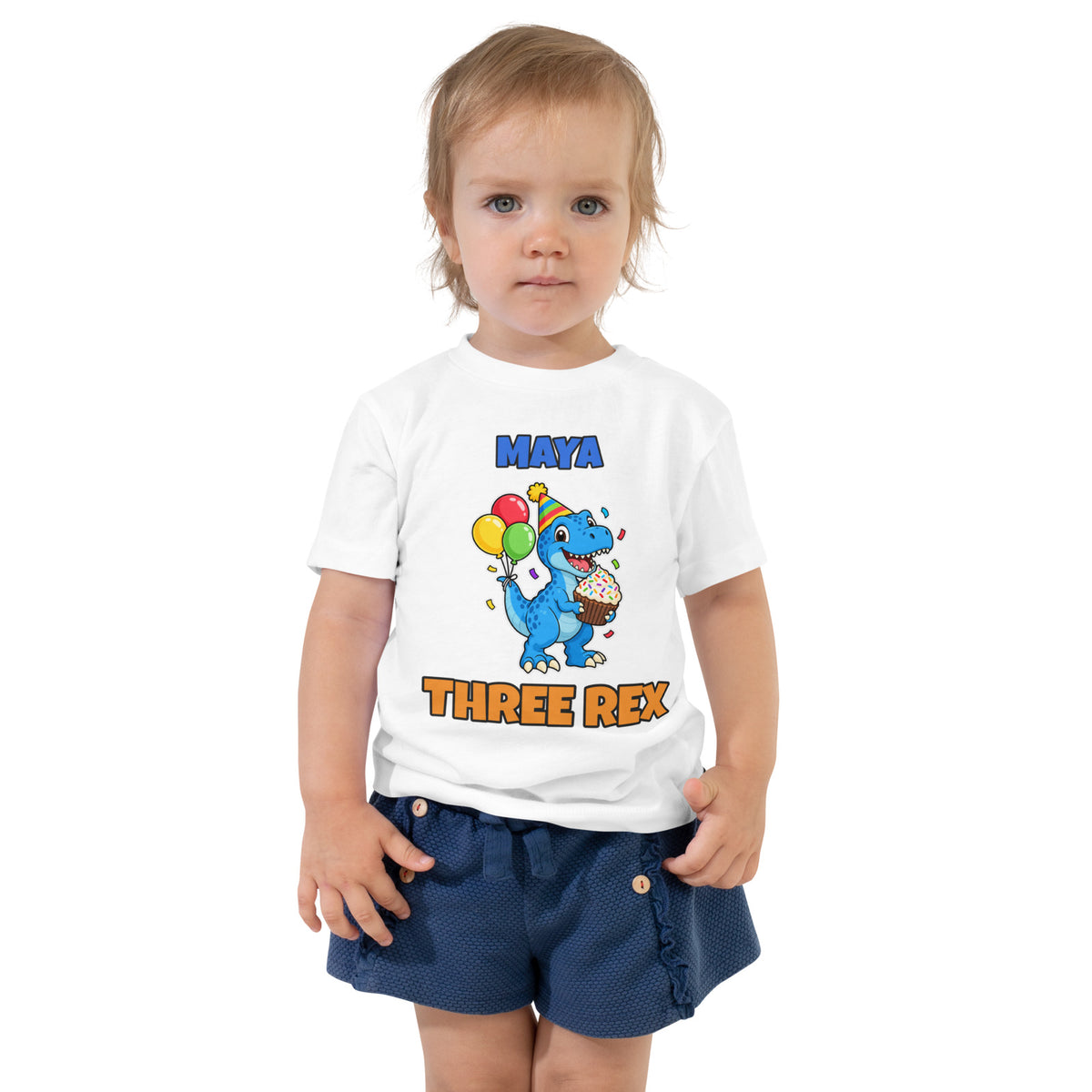 Birthday Rex personalized toddler dinosaur birthday t-shirt in White, blue party-hat T-rex with cupcake and balloons between the name MAYA and THREE REX, worn by a child, front view