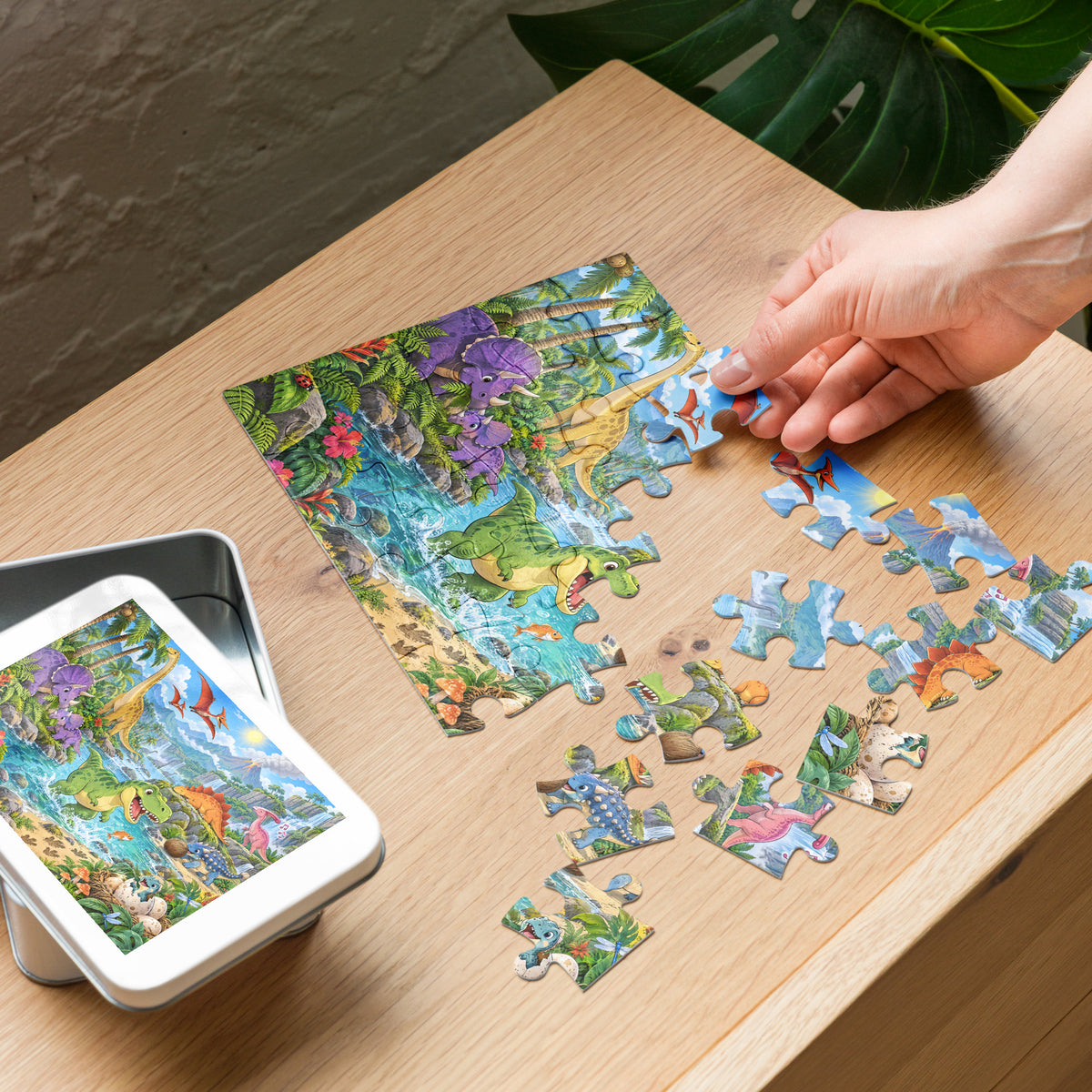 Building the Dino Valley dinosaur puzzle on a table next to its white metal gift tin with the picture on the lid